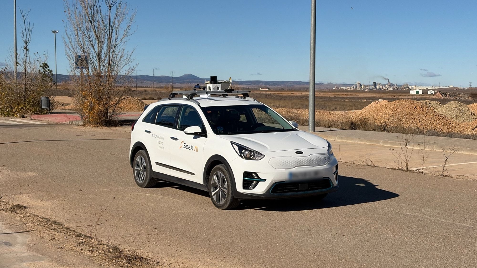 Nuestro vehículo, un coche eléctrico blanco con el LiDAR en el techo, en un vial asfaltado.