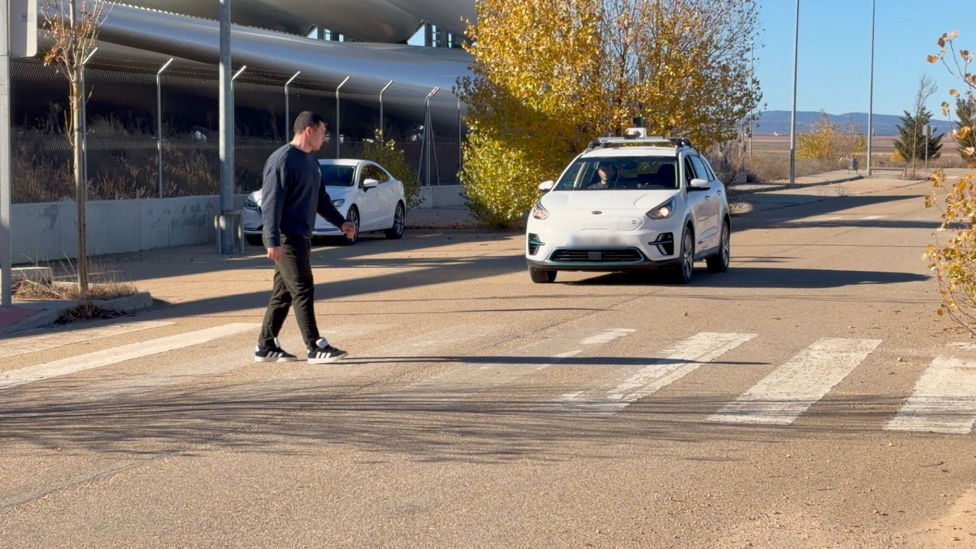 Nuestro vehículo, un coche blanco con el LiDAR en el techo, y una persona que cruza por delante durante una prueba en el Aeropuerto de Teruel.