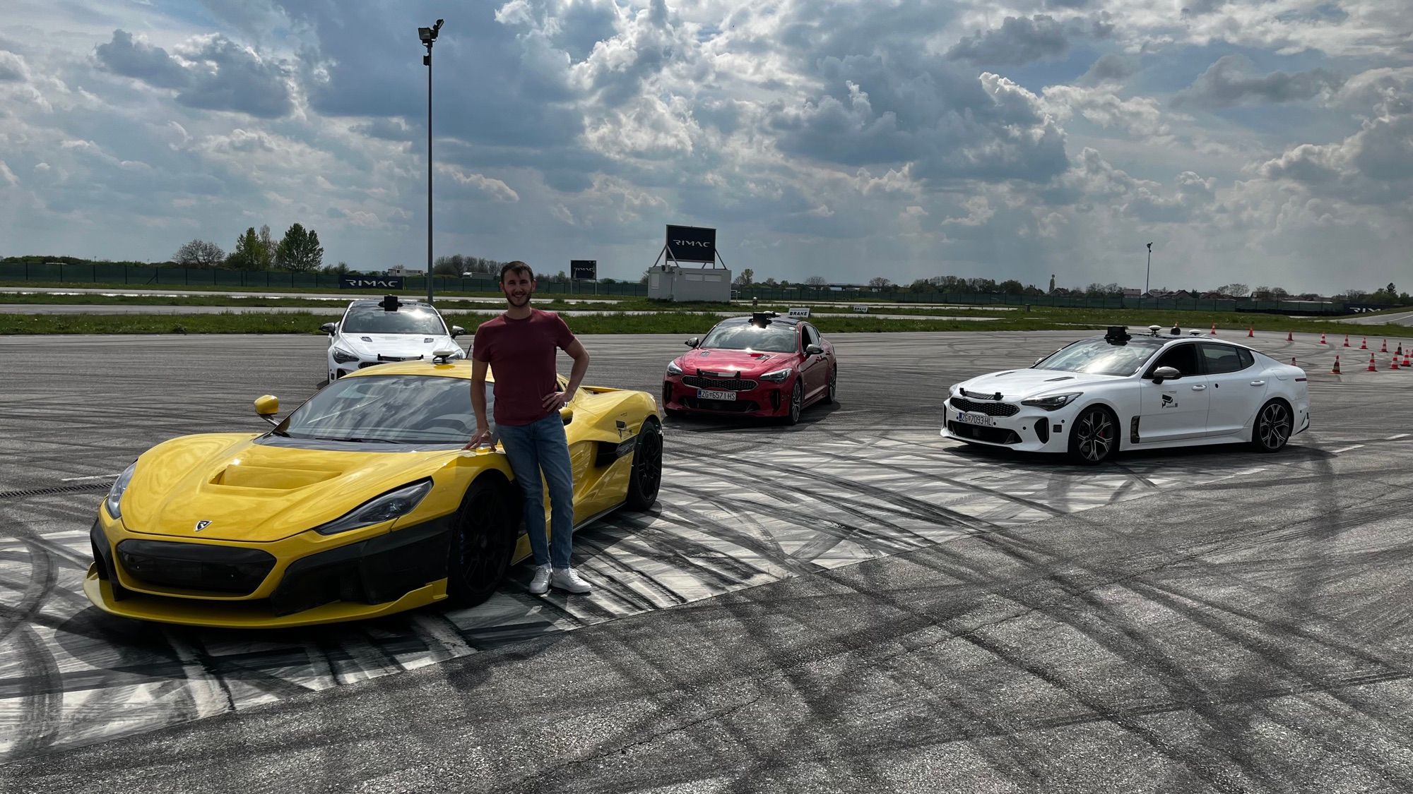 Eugenio Alcalá junto a un coche de RIMAC en una pista de pruebas, con otros vehículos al fondo.